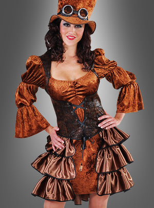 Eine Frau, die das Steampunk-Samtkleid im Stil einer echten viktorianischen Steampunk-Dame trägt – mit Puffärmeln, einem Rüschenrock, einem schwarzen Korsett und einem Zylinder mit Schutzbrille –, steht vor einem grauen Hintergrund.