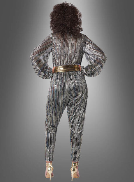 Eine Person steht mit dem Rücken zur Kamera und trägt den „Disco Kostüm Jumpsuit Super Nova“ mit Metallic-Streifen, kombiniert mit einem goldenen Gürtel und goldenen Stöckelschuhen, vor einem grauen Hintergrund mit Farbverlauf.