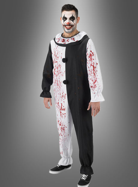Eine Person im „Terrifier“-Kostüm als Horrorclown „Art the Clown“ – ein schwarz-weißes Clownkostüm mit Blutflecken und passender Gesichtsbemalung –, die vor einem grauen Hintergrund steht und lächelt und dabei die gruselige Ausstrahlung von „Art the Clown“ aus „Terrifier“ einfängt; perfekt für jeden Fan von Horrorclowns.