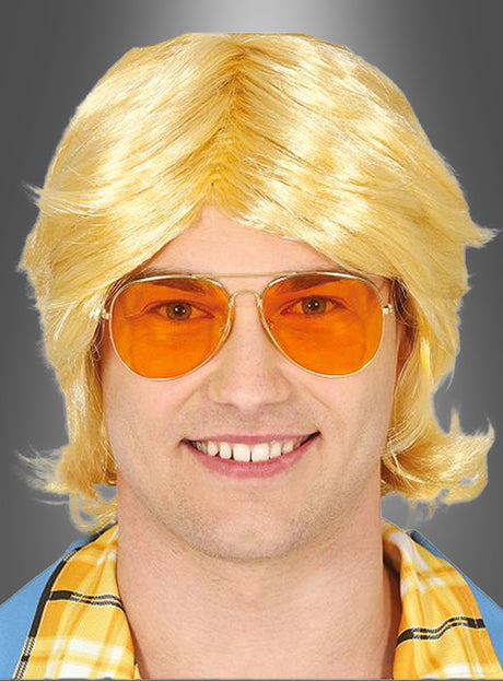 Ein Mann mit einer blonden Perücke, einer Retro-Brille aus den 70er Jahren mit orange getönten Pilotenbrillengläsern und einem gelben Karohemd lächelt vor einem grauen Hintergrund mit Farbverlauf in die Kamera.