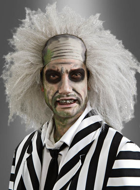 Eine Person in einem schwarz-weiß gestreiften Anzug mit wildem weißem Haar, blasser Haut und dunklem Augen-Make-up, die eine Beetlejuice-Perücke mit Stirnglatze trägt und vor einem grauen Hintergrund posiert.