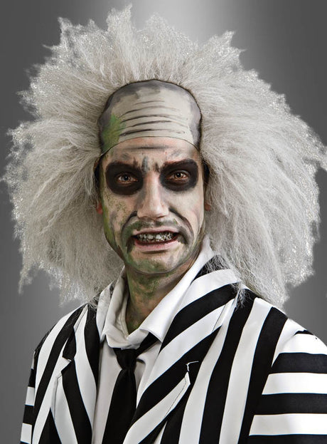 Eine Person in einem schwarz-weiß gestreiften Anzug mit wildem weißem Haar, blasser Haut und dunklem Augen-Make-up, die eine Beetlejuice-Perücke mit Stirnglatze trägt und vor einem grauen Hintergrund posiert.