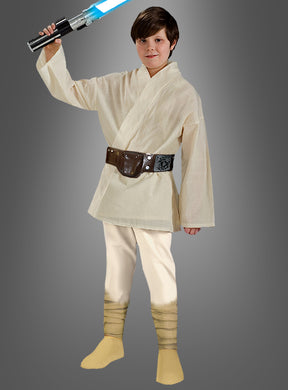 Ein Kind in einem „Deluxe Luke Skywalker“-Star-Wars-Kinderkostüm hält ein blaues Lichtschwert in der Hand und steht vor einem schlichten grauen Hintergrund.
