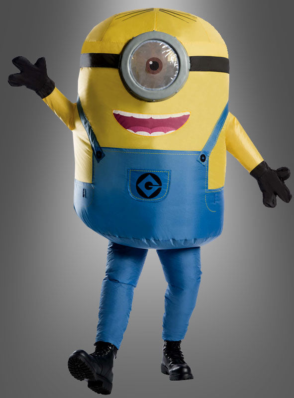 Eine Person, die das aufblasbare Minion-Kostüm „Stuart“ trägt – bestehend aus einem gelben Oberkörper, einer blauen Latzhose, einem großen Auge und schwarzen Handschuhen –, steht vor einem grauen Hintergrund.