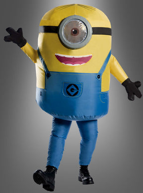 Eine Person, die das aufblasbare Minion-Kostüm „Stuart“ trägt – bestehend aus einem gelben Oberkörper, einer blauen Latzhose, einem großen Auge und schwarzen Handschuhen –, steht vor einem grauen Hintergrund.