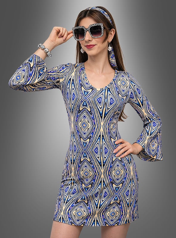 Eine Frau posiert vor einem schlichten grauen Hintergrund in einem Paillettenkleid im 70er-Jahre-Disco-Stil mit Accessoires, darunter ausgestellte Ärmel, eine übergroße Sonnenbrille, ein passendes Stirnband und ein silbernes Armband.