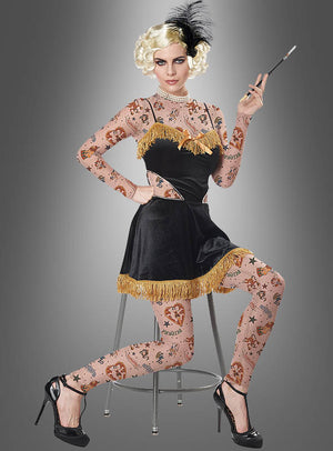 Eine Frau mit einer blonden Perücke und einem Kleid im Flapper-Stil trägt das „Erstaunliche Tattoo Dame“-Kostüm, sitzt auf einem Hocker und hält eine Zigarettenspitze in der Hand, vor einem grauen Hintergrund mit Farbverlauf.