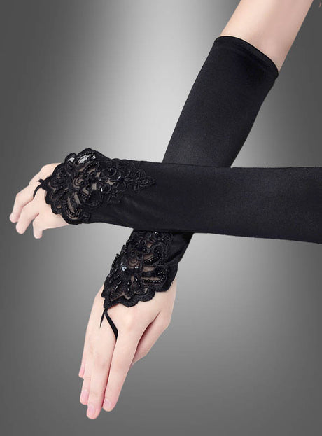 Zwei am Handgelenk gekreuzte Hände tragen „Fingerlose Handschuhe lang mit Spitze“ mit aufwendigen Spitzen- und Perlenverzierungen an den Bündchen vor einem grauen Hintergrund mit Farbverlauf. Diese eleganten „Fingerlose Handschuhe lang mit Spitze“ verleihen jedem Outfit einen Hauch von Raffinesse.