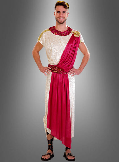 Vor einem grauen Hintergrund steht ein Mann in einem Kostüm im römischen Stil mit einer weißen Tunika, einer roten Schärpe, goldenen Verzierungen und schwarzen Sandalen.