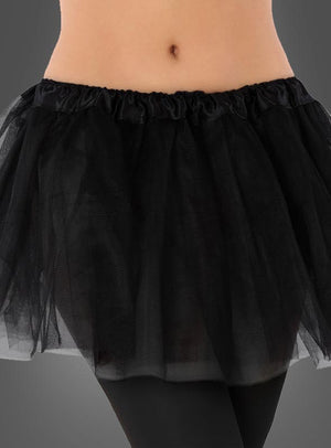 Vor einem grauen Hintergrund ist eine Person zu sehen, die den „Tütü Kinder Tüllrock“ trägt, einen kurzen schwarzen Tutu-Rock, kombiniert mit schwarzen Leggings und einem bauchfreien Oberteil.