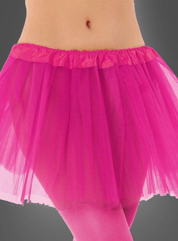 Eine Person, die den „Tütü Kinder Tüllrock“ – einen leuchtend pinkfarbenen Tüll-Tutu-Rock – sowie eine pinkfarbene Strumpfhose trägt, fotografiert von der Taille bis zur Mitte des Oberschenkels vor einem grauen Hintergrund.