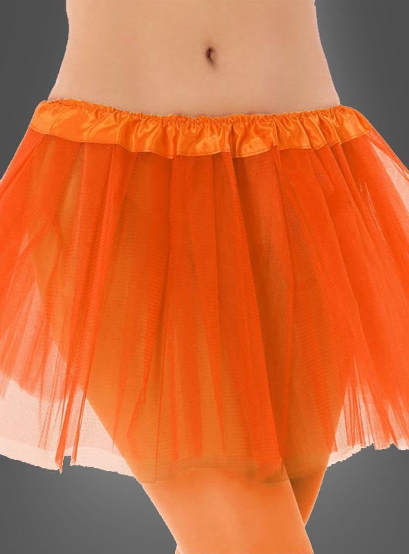 Eine Person, die einen kurzen, orangefarbenen „Tütü Kinder“-Tüllrock mit einem Satinbund trägt, steht vor einem schlichten, dunklen Hintergrund.