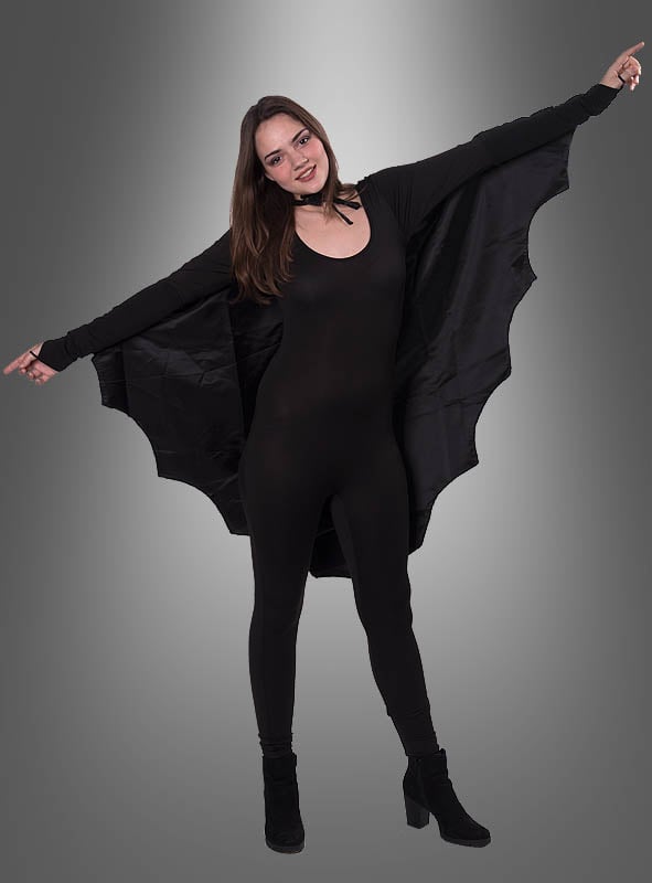 Eine Frau, die das „Fledermaus“-Cape für Damen und Herren trägt, steht mit ausgestreckten Armen da und präsentiert den flügelartigen Stoff vor einem grauen Hintergrund mit Farbverlauf – eine auffällige Wahl für ein Halloween-Kostüm für Damen.