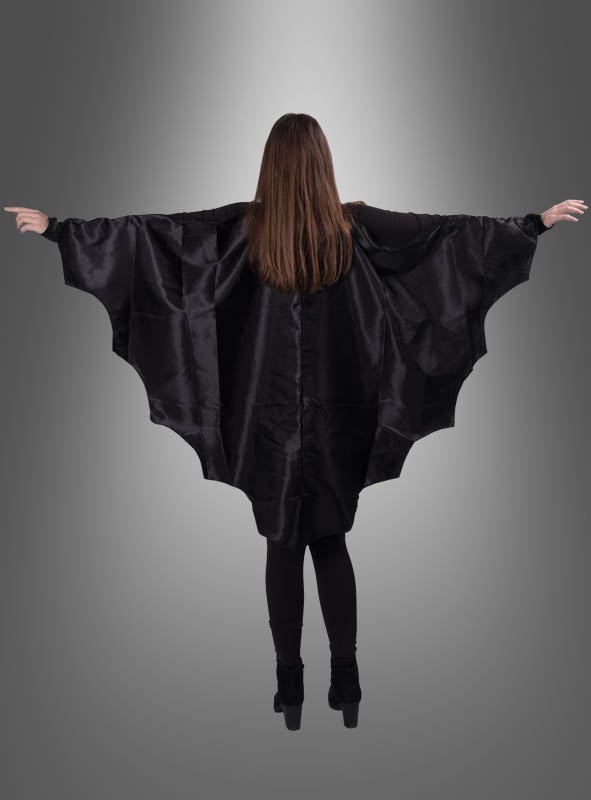 Eine Person mit langen braunen Haaren steht mit ausgestreckten Armen da, trägt den „Fledermaus-Umhang für Damen und Herren“ in einem auffälligen Halloween-Stil und blickt mit dem Rücken zu einem grauen Hintergrund mit Farbverlauf.