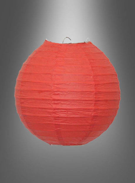 Ein runder roter „Papierlampion in kräftigen Farben (20–45 cm)“ mit einem stabilen Metallrahmen ist vor einem grauen Hintergrund mit Farbverlauf aufgehängt und eignet sich somit ideal als Partydekoration für Ihre nächste Gartenparty.