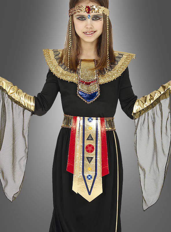 Ein Kind posiert vor einem grauen Hintergrund und trägt das „Ägyptische Prinzessin“-Kinderkostüm, ein Kostüm für Mädchen im ägyptischen Stil, das mit goldenen, roten und blauen Akzenten verziert ist. Das Outfit verfügt über einen breiten Kragen, einen Ziergürtel und transparente schwarze Ärmel, wodurch es an den majestätischen Look eines Pharaonin-Kostüms erinnert und die Eleganz des antiken Königshauses einfängt.