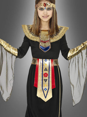 Ein Kind posiert vor einem grauen Hintergrund und trägt das „Ägyptische Prinzessin“-Kinderkostüm, ein Kostüm für Mädchen im ägyptischen Stil, das mit goldenen, roten und blauen Akzenten verziert ist. Das Outfit verfügt über einen breiten Kragen, einen Ziergürtel und transparente schwarze Ärmel, wodurch es an den majestätischen Look eines Pharaonin-Kostüms erinnert und die Eleganz des antiken Königshauses einfängt.
