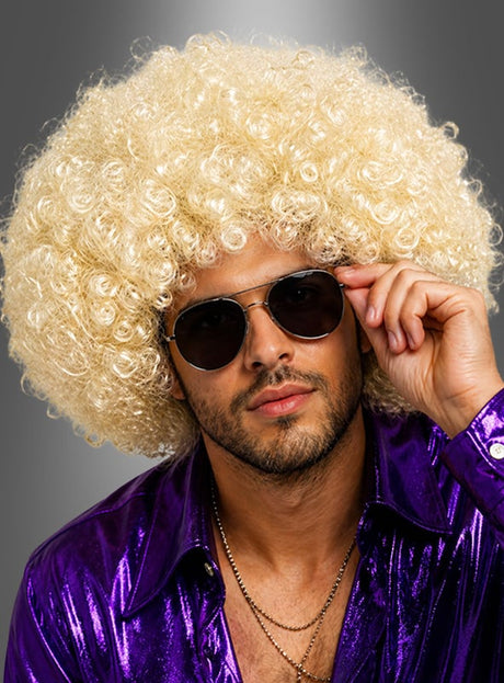Ein Mann mit der blonden Lockenperücke „Super Riesen Afroperücke Deluxe Unisex“, einer Pilotenbrille und einem glänzenden lila Hemd posiert vor einem grauen Hintergrund – perfekt für jede 70er-Jahre-Kostümparty.