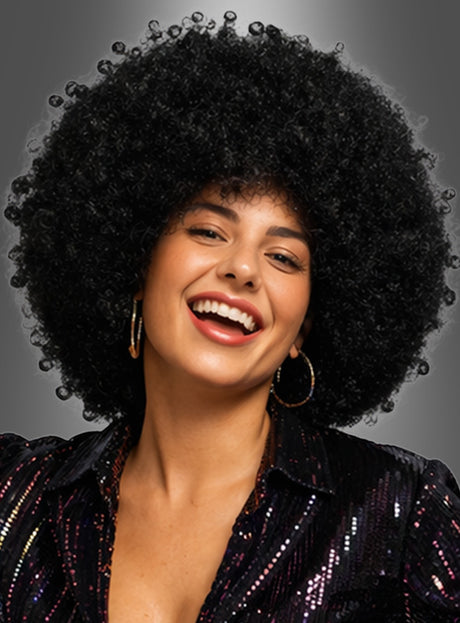 Eine Frau mit einer voluminösen, lockigen Afro-Frisur, die an die „Super Riesen Afroperücke Deluxe Unisex“ erinnert, trägt Creolen und ein glänzendes schwarzes Oberteil und lächelt vor einem grauen Hintergrund.