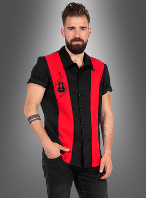 Ein bärtiger Mann, der ein schwarzes, kurzärmeliges „Rockabilly Hemd Dean“-Shirt mit roten vertikalen Streifen und einem Gitarrenmotiv trägt, steht vor einem grauen Hintergrund mit Farbverlauf.