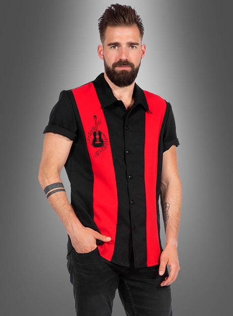 Ein bärtiger Mann, der ein schwarzes, kurzärmeliges „Rockabilly Hemd Dean“-Shirt mit roten vertikalen Streifen und einem Gitarrenmotiv trägt, steht vor einem grauen Hintergrund mit Farbverlauf.