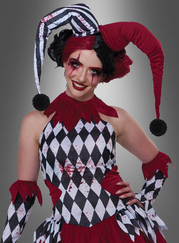 Eine Person, die als „Verrückte Harlekin-Dame Topsy“ verkleidet ist und ein rot-schwarzes Harlekin-Kostüm sowie eine auffällige rot-schwarze Gesichtsbemalung trägt, posiert vor einem schlichten grauen Hintergrund mit Farbverlauf.
