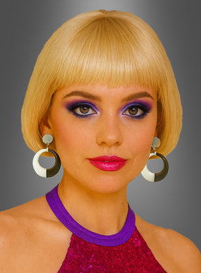 Eine Frau mit einem kurzen blonden Bob, auffälligem lila Augen-Make-up, rosa Lippenstift und großen runden GoGo-Ohrringen in Schwarz-Weiß sowie einem lila Top mit Pailletten verkörpert vor einem grauen Hintergrund mit Farbverlauf den lebhaften Geist eines Go-Go-Mod-Kostüms.