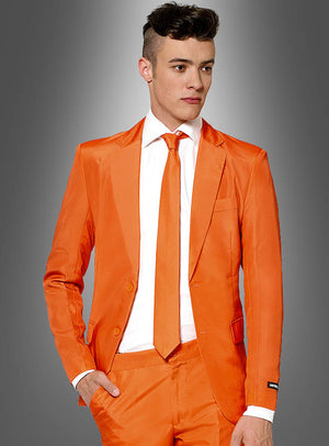 Ein Mann, der einen leuchtend orangefarbenen Herrenanzug von „Orange Suitmeister“ mit einer orangefarbenen Krawatte und einem weißen Hemd trägt, steht vor einem grau abgestuften Hintergrund und präsentiert einen markanten und stilvollen Look, der an das einzigartige Flair der Suitmeister-Kollektionen erinnert.