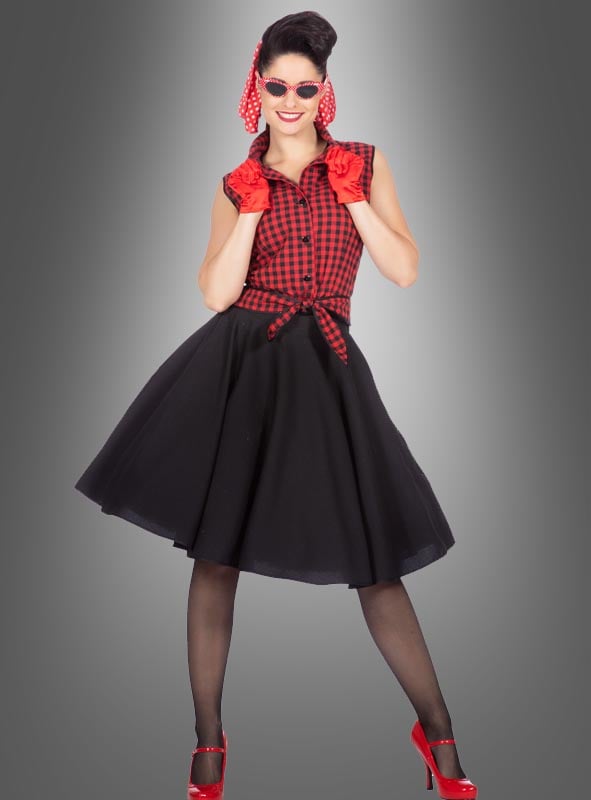 Eine Frau posiert vor einem grauen Hintergrund mit Farbverlauf und trägt das Rockabilly-Kleid „Rizzo“ im Stil der 50er Jahre – ein rotes kariertes Oberteil mit einem schwarzen, ausgestelltem Rock und einem Unterrock –, kombiniert mit einer schwarzen, transparenten Strumpfhose, roten Pumps, roten Handschuhen, einem roten Schal und einer Sonnenbrille.
