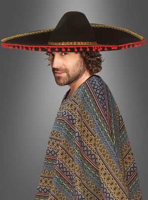 Ein Mann, der einen gemusterten Poncho und einen großen schwarzen Sombrero „Hut XXL Mexikaner“ (ca. 55 cm Umfang) mit roter und goldener Verzierung trägt und vor einem neutralen grauen Hintergrund steht.