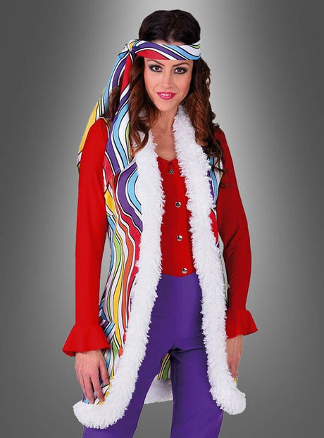 Eine Frau in einem farbenfrohen Retro-Outfit mit der „Hippie Weste Rainbow“, kombiniert mit einem roten Oberteil, einer lila Hose und einem dazu passenden gestreiften Stirnband, steht vor einem schlichten grauen Hintergrund.
