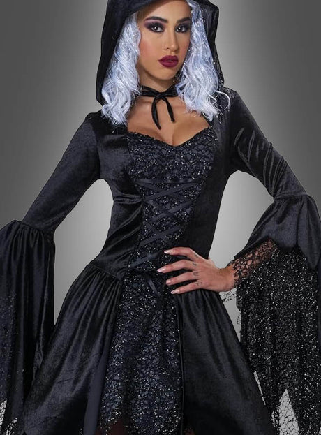 Eine Person, die das „Schwarze Glamour-Hexe-Kleid mit Kapuze“ trägt – ein schwarzes Kleid mit Kapuze, ausgestellten Ärmeln und zarten Spitzendetails –, posiert elegant vor einem grauen Hintergrund.