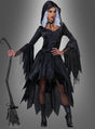 Eine Person, die ein schwarzes Glamour-Hexenkleid mit Kapuze trägt, dazu eine Kapuze, eine silberne Perücke und ausgestellte Ärmel, und die einen Besen in der Hand hält, steht vor einem grauen Hintergrund.