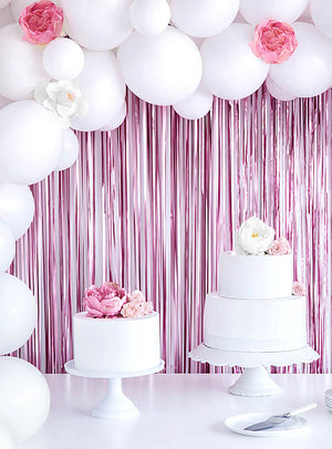 Auf Tortenständern stehen zwei weiße Torten mit rosa und weißen Blumen; im Hintergrund schimmert ein „Party Deko Lametta-Vorhang 250 cm“, der die festliche Dekoration perfekt ergänzt.