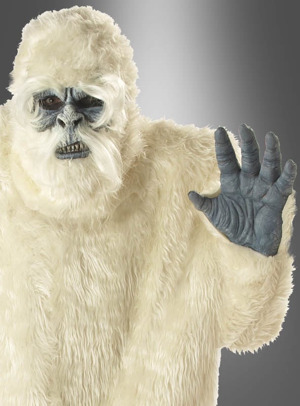 Eine Person, die das Yeti-Kostüm für Erwachsene trägt – mit einem weißen, pelzigen Körper, einem grauen Gesicht und grauen Händen –, hebt eine Hand und blickt vor einem neutralen Hintergrund nach vorne.