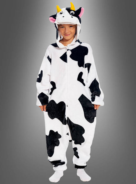 Ein Kind, das den „Kuh-Overall für Kinder“ trägt – einen schwarz-weißen Overall mit Kuhmuster, Kapuze, Kuhöhrchen und gelben Hörnern, der sich perfekt als Kuscheloverall oder Kuhkostüm für Kinder eignet –, steht vor einem grauen Hintergrund.