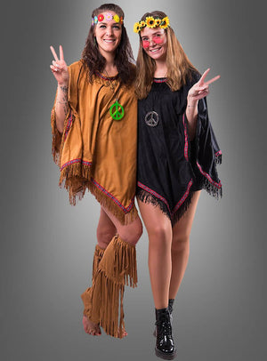 Zwei Frauen in Hippie-Kostümen, mit Blumenstirnbändern und Halsketten mit Peace-Zeichen, lächeln und zeigen vor einem grauen Hintergrund das Peace-Zeichen. Ihre farbenfrohen Outfits strahlen Retro-Flair aus, wobei verspielte Details wie der „Wandelbare Poncho mit Fransen Hippie Indianer“ ihrem Look einen zusätzlichen Hauch von nostalgischem Charme verleihen.