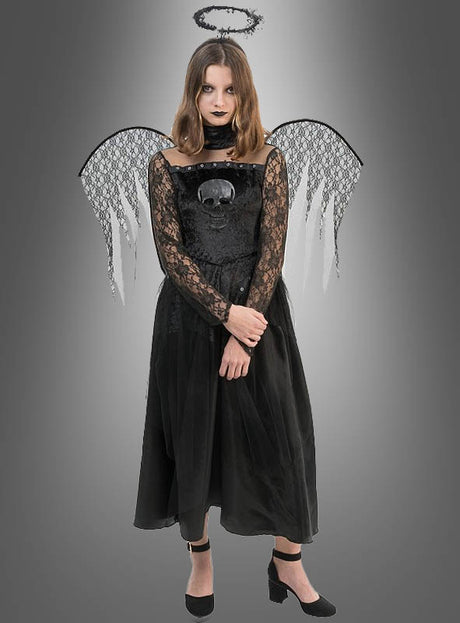 Eine Frau, die ein „Todesengel“-Spitzenkleid für Mädchen mit Totenkopf-Motiv, schwarzen Engelsflügeln, einem schwarzen Heiligenschein und schwarzen Schuhen trägt, steht vor einem grauen Hintergrund mit Farbverlauf.