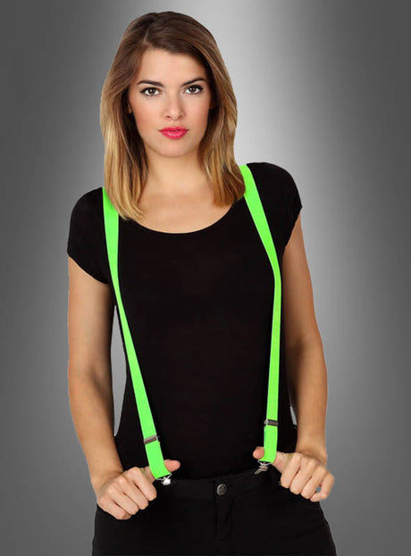 Eine Frau in einem schwarzen Shirt und stylischen Neon-Hosenträgern in tollen Farben steht vor einem grauen Hintergrund mit Farbverlauf und hält die leuchtend grünen Hosenträger mit beiden Händen fest – ein Ausdruck des auffälligen Stils, der perfekt zu jeder 80er- und 90er-Jahre-Party passt.