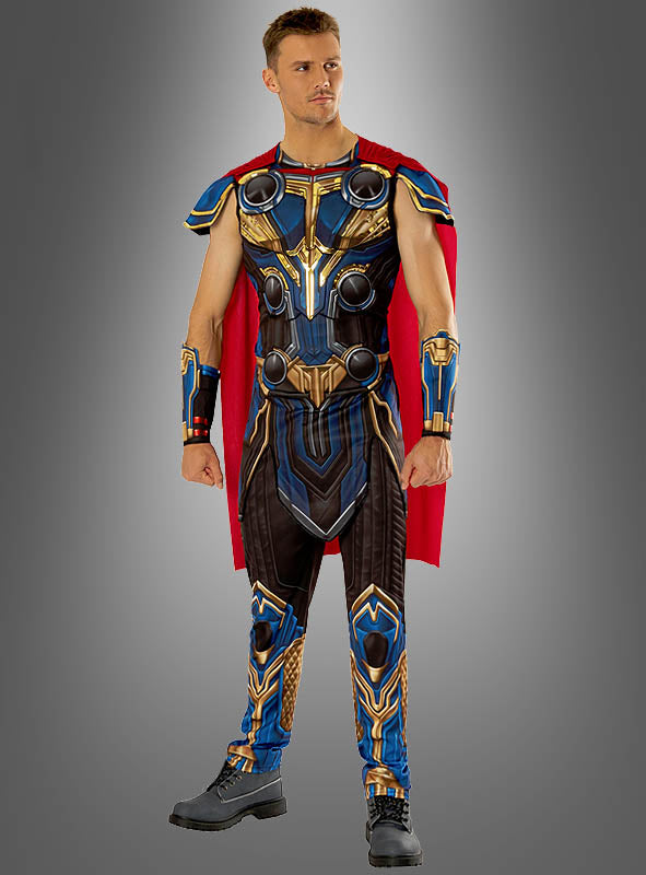 Ein Mann, der das „Thor Deluxe-Kostüm, 2-teilig für Männer“ trägt – ein blau-goldenes Superheldenkostüm mit rotem Umhang und Stiefeln –, steht vor einem grauen Hintergrund mit Farbverlauf und verkörpert damit perfekt den legendären Marvel-Look.