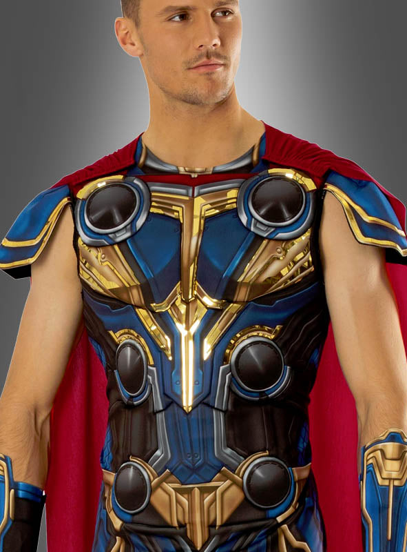 Eine Person, die das „Thor Deluxe“-Kostüm (2-teilig für Männer) trägt – das sich durch eine aufwendig gearbeitete goldene, blaue und rote Rüstung sowie einen leuchtend roten Umhang auszeichnet –, steht selbstbewusst vor einem grauen Hintergrund.