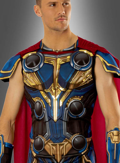 Eine Person, die das „Thor Deluxe“-Kostüm (2-teilig für Männer) trägt – das sich durch eine aufwendig gearbeitete goldene, blaue und rote Rüstung sowie einen leuchtend roten Umhang auszeichnet –, steht selbstbewusst vor einem grauen Hintergrund.