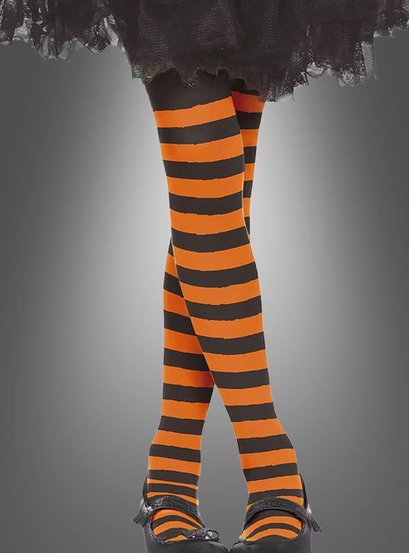 Ein Kind in einer orange-schwarzen „Kinder Ringelstrumpfhose“, schwarzen Schuhen mit Schleifen und einem schwarzen Rüschenrock vor grauem Hintergrund – perfekt für ein verspieltes Kostüm.