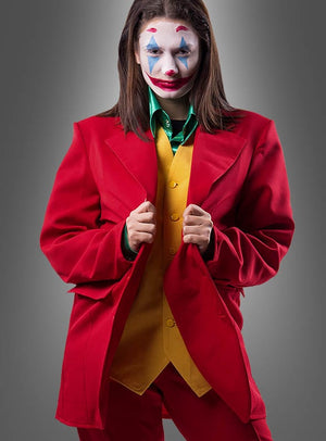 Eine Person mit Clown-Make-up, die das „Roter Anzug für Joker“-Outfit trägt – komplett mit gelber Weste und grünem Hemd –, steht vor einem grauen Hintergrund und verkörpert damit den unverwechselbaren Stil und den markanten Charakter des legendären Joker-Looks.