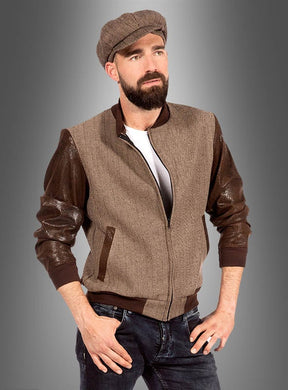 Ein bärtiger Mann trägt eine braune Schirmmütze, die Vintage-Herrenjacke „Duke Rockabilly“ in Braun und Beige, ein weißes T-Shirt und Jeans und steht mit den Händen in den Taschen vor einem grauen Hintergrund mit Farbverlauf.