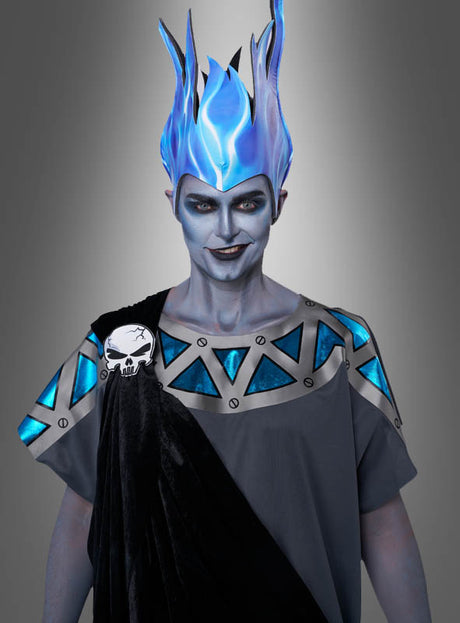 Eine Person, die das „Herrscher der Unterwelt“-Kostüm für Herren trägt – inspiriert von einem Hades-Kostüm und bestehend aus einem blauen, flammenartigen Kopfschmuck, einer grau-blauen Robe mit geometrischen Mustern sowie einer Totenkopf-Anstecknadel –, steht vor einem grauen Hintergrund mit Farbverlauf.
