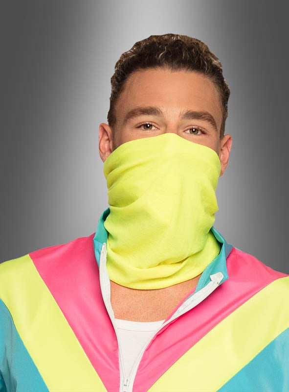 Ein Mann, der einen neongelben Mund-Nasen-Schutz und den „80er Trainingsanzug blau“ mit leuchtend pinken, türkisfarbenen und gelben Streifen trägt, posiert vor einem grauen Hintergrund mit Farbverlauf.