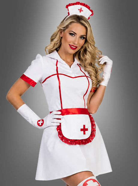 Eine Frau im sexy „Krankenschwester Betty“-Kostüm, bestehend aus einem weißen Kleid mit roten Akzenten, einer passenden Mütze, Handschuhen und einer kleinen Schürze, posiert vor einem grauen Hintergrund.