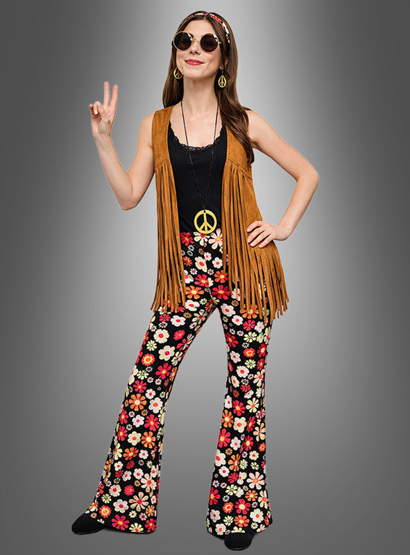 Im Stil der 1970er Jahre rockt diese Frau das Hippie-Kostüm mit Accessoires „Night Flower“: ein Retro-Outfit bestehend aus einer Weste mit Fransen, einer geblümten Schlaghose, einem schwarzen Oberteil, einer Halskette mit Peace-Zeichen und einer Sonnenbrille. Dabei posiert sie mit einer Handgeste, die das Peace-Zeichen darstellt.