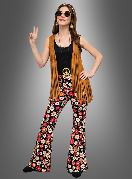 Im Stil der 1970er Jahre rockt diese Frau das Hippie-Kostüm mit Accessoires „Night Flower“: ein Retro-Outfit bestehend aus einer Weste mit Fransen, einer geblümten Schlaghose, einem schwarzen Oberteil, einer Halskette mit Peace-Zeichen und einer Sonnenbrille. Dabei posiert sie mit einer Handgeste, die das Peace-Zeichen darstellt.
